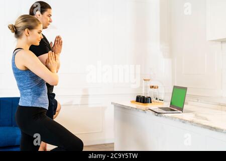 White caucasian fit sporty couple doing yoga tree pose in living room at home watching online tutorials from trainer on laptop. Working out, fitness s Stock Photo
