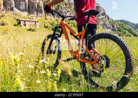 detail the wheels of a mountain bike and the legs of a cyclist walking through a flower meadow, concept of sport and healthy lifestyle in nature Stock Photo