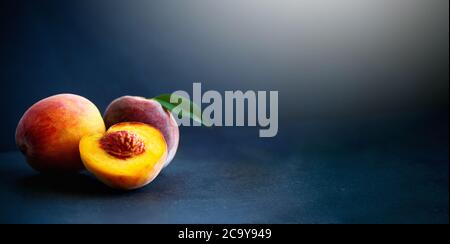 Fresh peaches and split with leaves on black background. Stock Photo