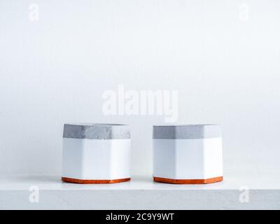 Two empty modern geometric concrete planters decoration on white shelf isolated on white wall background with copy space. Beautiful painted hexagon ce Stock Photo