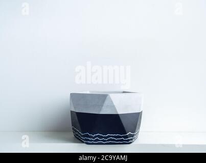 Empty modern geometric concrete planter on white shelf isolated on white wall background with copy space. Beautiful black colour painted cement pot. Stock Photo
