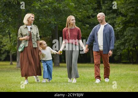 Full length portrait of modern family with two kids holding hands while walking towards camera on green grass outdoors, copy space Stock Photo