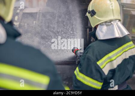 Fireman holding fire hose nozzle and splashing water Stock Photo