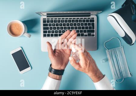 Stay safe, businessman using disinfectant spray in office while working on laptop computer, top view image Stock Photo