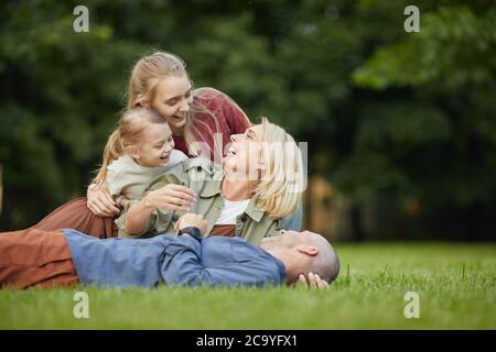 Portrait of happy modern family lying on green grass in park while having fun together outdoors, copy space Stock Photo