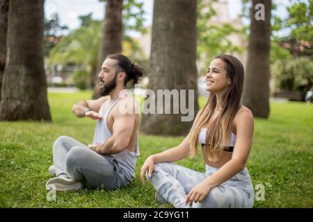 People Sport and lifestyle concept - Relaxed couple of travelers, making yoga exercises, meditating, breathing outdoors in the hotel exotic garden spa Stock Photo