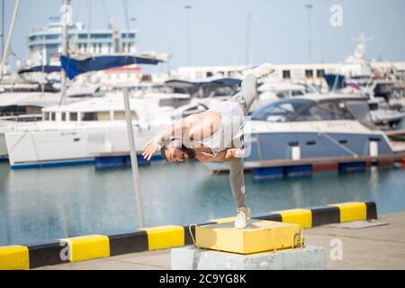 Muscular caucasian athlete increasing power with plyometric workout, doing extreme flip jumps at ocean pier or embankment, near seaside Stock Photo