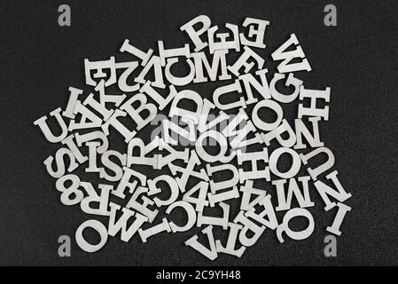 Letters of English alphabet arranged in chaotic order on black background. Top wiev. Stock Photo