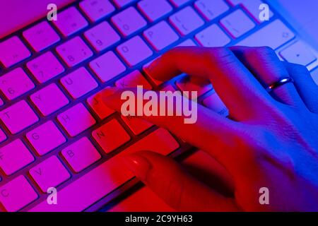 Woman working on laptop computer from home. Business  people lifestyle. Woman typing on laptop computer in blue and pink tones. Woman hand typing mess Stock Photo