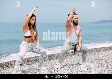 Professional female boxer or fighter and her trainer warming out outdoors, doing taekwondo exercise together on the ocean pebble beach with sea surf a Stock Photo