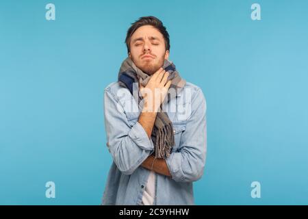 Portrait of unhealthy flu-sick man standing wrapped in warm scarf shivering from cold, feeling unwell suffering fever, seasonal influenza symptoms. in Stock Photo