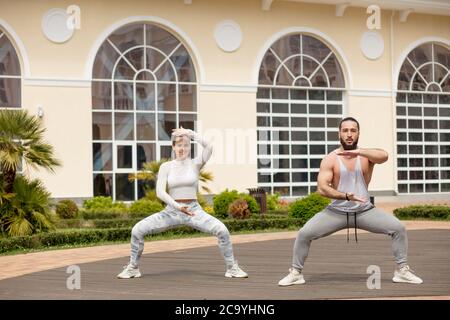 Sporty couple doing squat for exercising thigh muscle in front of fitness centre entrance outdoor Stock Photo
