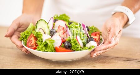 Vegetable salad in white dish holding woman hands. Stock Photo