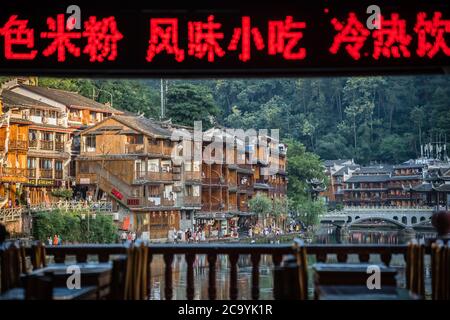 Feng Huang, China -  August 2019 : Chinese characters in red flickering on the display above the tables on the balcony in a riverside view restaurant Stock Photo