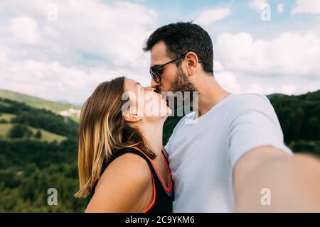 Young couple taking a selfie while kissing in the mountains Stock Photo