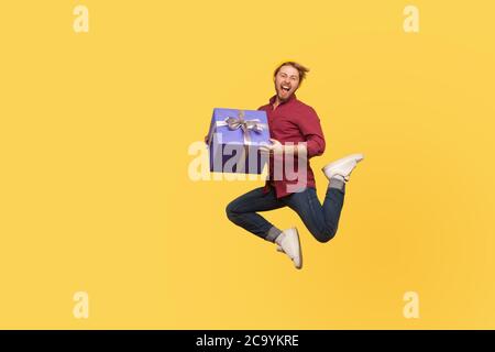 Enthusiastic extremely joyful hipster guy jumping trampoline with gift box, flying in air holding birthday present surprise, enjoying holiday bonus. f Stock Photo