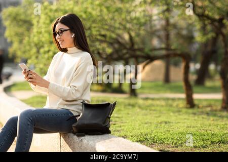 Female student using phone, sitting in the park Stock Photo