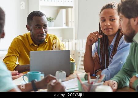 Portrait of creative African-American man using laptop while working on team project with multi-ethnic group of people, copy space Stock Photo