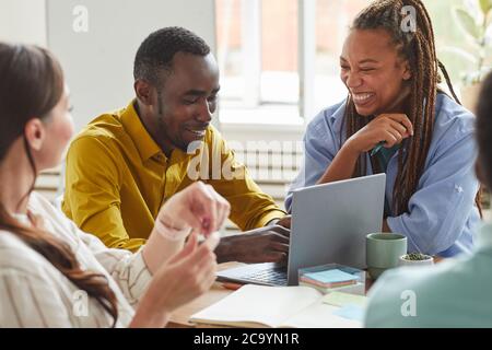 Portrait of African-American man and woman laughing cheerfully while working on team project with multi-ethnic group of people, copy space Stock Photo