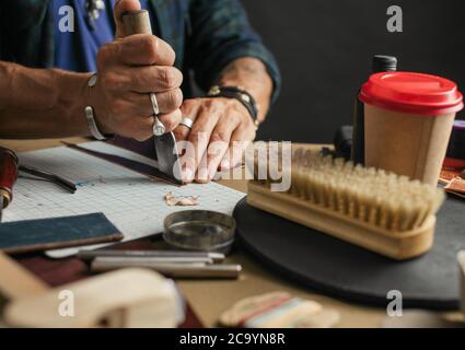 Leather goods master hands cutting piece of natural leather with crafting tool. Workflow in the workshop. Workflow in the workshop, close-up. Stock Photo
