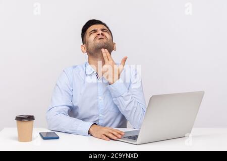 Upset depressed male employee sitting office workplace with laptop on desk, pointing finger gun gesture to head, committing suicide from stressful job Stock Photo