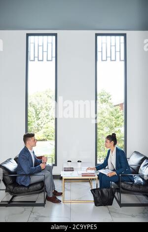 Young business partners meeting in lounge room of office building and discussing financial reports and contact details Stock Photo