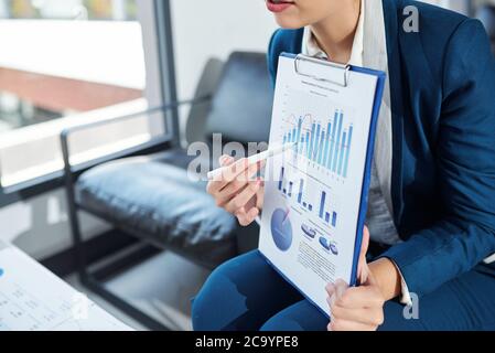 Cropped image of businesswoman pointing at bar chart in financial report when talking at meeting Stock Photo