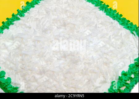 Birthday cake decorated with green icing and grated coconut. Isolated on yellow background. Top view. Close-up. Stock Photo