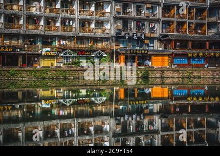 Feng Huang, China -  August 2019 : Reflection of traditional old wooden houses on the riverbanks of Tuo river, flowing through the centre of Feng huan Stock Photo