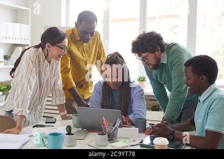 Portrait of contemporary multi-ethnic team leaning over laptop and smiling while working together in office, copy space Stock Photo