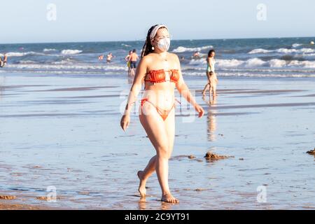 Punta Umbria, Huelva, Spain - August 2, 2020: Young Woman walking by the beach wearing protective or medical face masks. New normal in Spain with soci Stock Photo