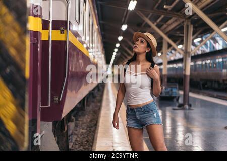 Confident young Hispanic brunette woman looking at train carriage on station platform, Hua Lamphong Station, Bangkok, Thailand Stock Photo
