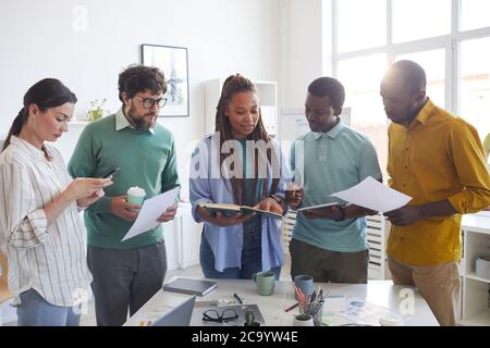 Portrait of contemporary multi-ethnic business team standing around table in office and listening to female African-American leader giving instructions, copy space Stock Photo