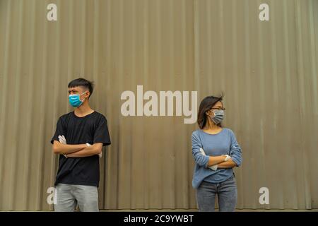 Asian young couple wearing a protective hygiene mask over her face to protect flu and virus. Unwell influenza in infected cpuple with light brown back Stock Photo
