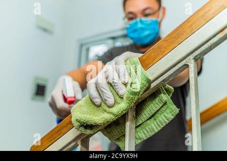 Young asian man in protective gloves disinfecting stair railings while cleaning at home, close-up view on hands and using spray bottle. Healthcare and Stock Photo