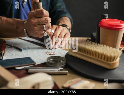 Handmade leather artisan making craft wallet using piece of natural leather on his working place with coffee and polishing brush , close up photo of h Stock Photo
