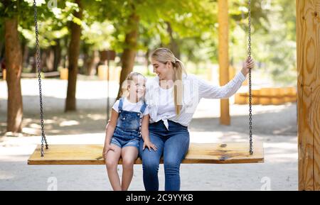 Mother And Little Daughter Swinging On Swings On Outdoor Playground Stock Photo