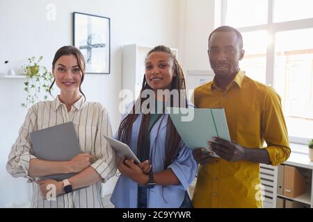 Waist up portrait of contemporary business team holding folders with documents and looking at camera while posing in office lit by sunlight, copy space Stock Photo