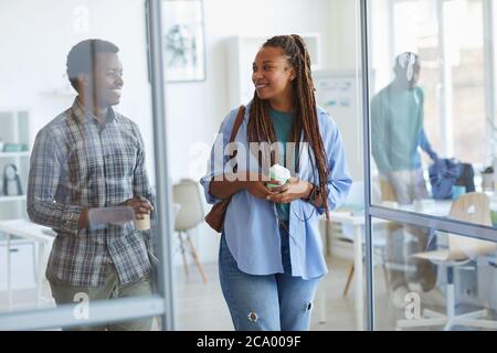 Portrait of contemporary African-American woman leaving office and smiling while walking through glass door, copy space Stock Photo