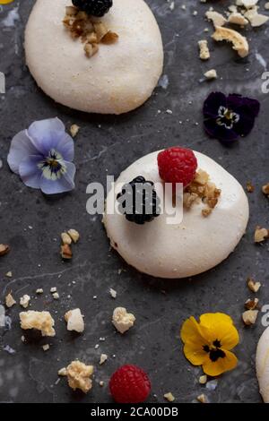 Aquafaba Meringues topped with edible flowers, crushed walnuts, blackberries and raspberries Stock Photo