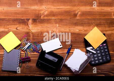 Stationery and calculator. Paper clips of different colors and elastics on wooden background, copy space. Business cards, notebook, puncher by binder, pins and sticky notes. Business idea concept. Stock Photo