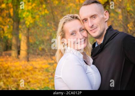 Lovely middle-aged couple in autumn park. Smiling man and woman hugged on fall background. Couple having fun in colorful autumn park. Happy pair on fa Stock Photo