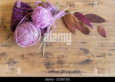 Flat lay of wool knitting and leaves with copy space on rustic wooden table. Knitted sock, ball of yarn, knitting needles, and leaves on rustic table. Stock Photo