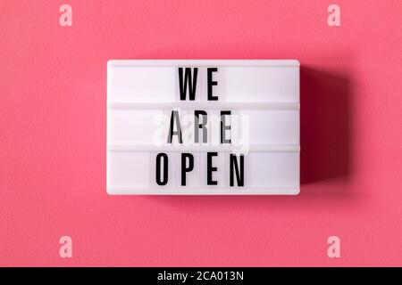 Signboard WE ARE OPEN of lightbox on red background. Open sign hanging on blue wall. Business open and welcome. Opening sign of cafe, bar, or restaura Stock Photo
