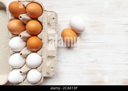 Brown and white eggs in recycled cardboard box and two chicken eggs near on wood table. Free-range organic eggs in paper box. Carton container with eg Stock Photo
