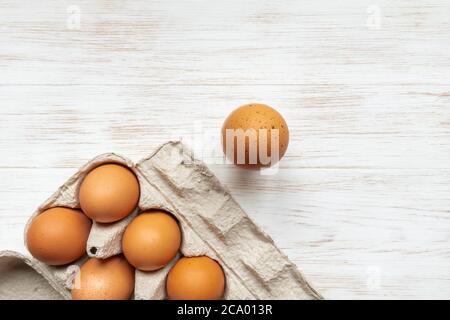 Free-range organic eggs in cardboard box. Close-up brown eggs in recycled cardboard box and one near on wood background. Carton container with brown c Stock Photo