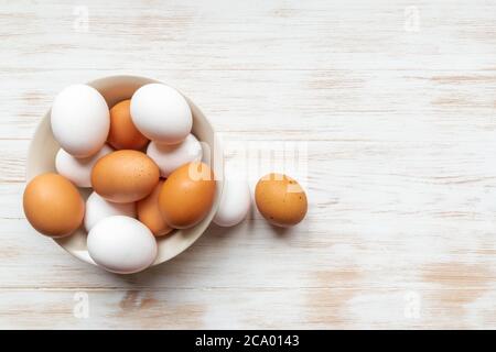 Brown and white eggs in plate and two near on wood background. Free-range organic eggs in bowl. Bowl with brown and white chicken eggs on wooden table Stock Photo