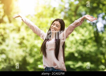 I Love Life. Asian Girl Sincerely Smiling And Raising Hands In Park Stock Photo