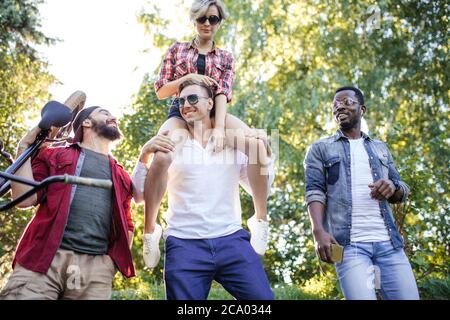 Portrait of confident university students on campus close up, best friends going to park picnic zone with happy woman rides piggyback - Happy youth fr Stock Photo