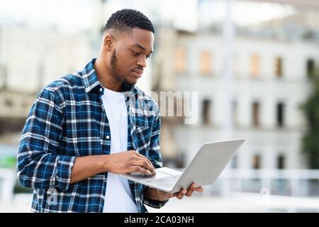 Black man using laptop, standing in city Stock Photo